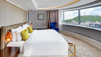 Una habitación de hotel con una cama grande, una silla, vistas a la ciudad y una obra de arte enmarcada en la pared.