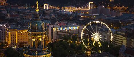A cityscape with a prominent domed building, a large Ferris wheel, and a bridge in the background.