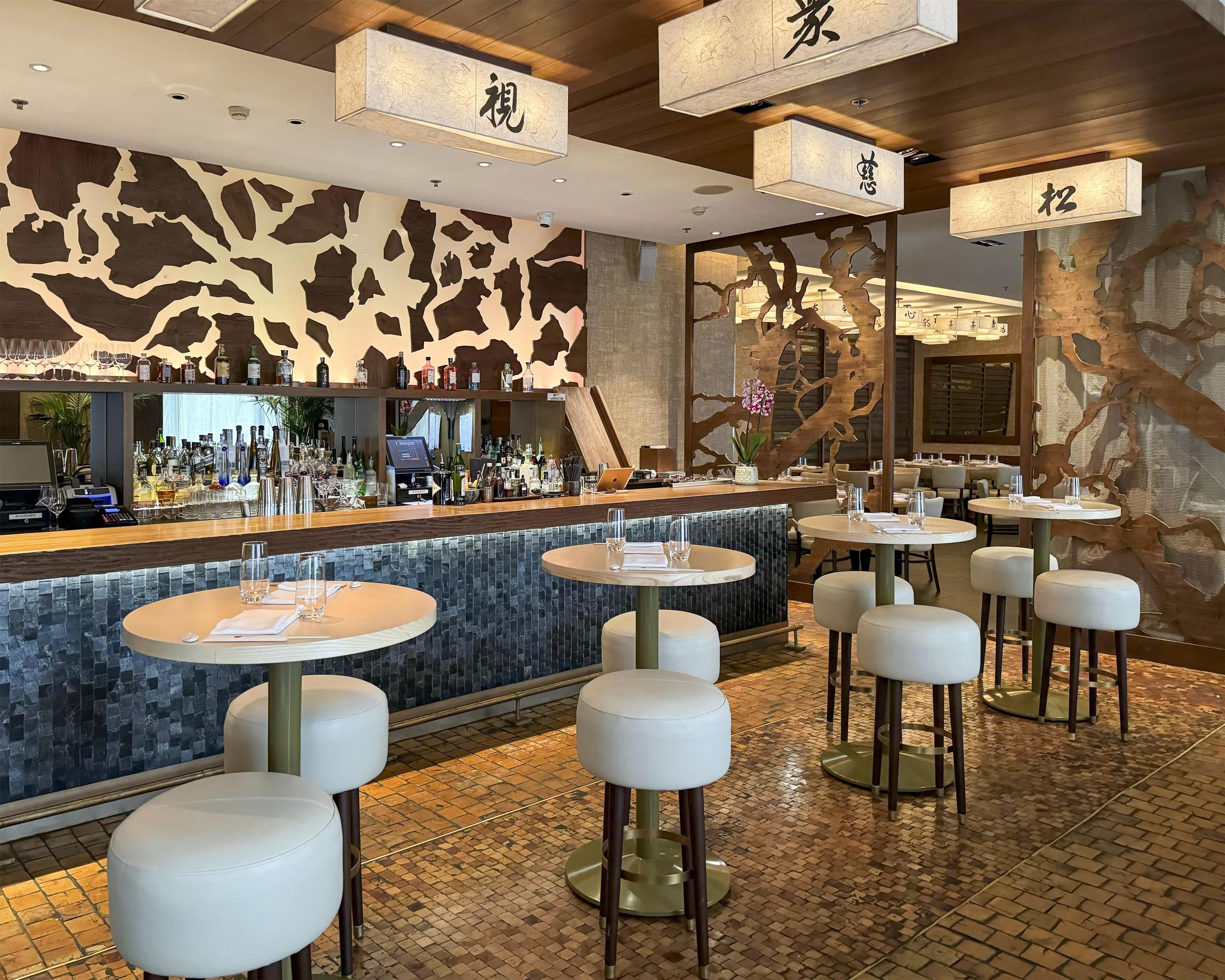 Uma área de bar com balcão, banquetas e um espaço de estar com mesas redondas.