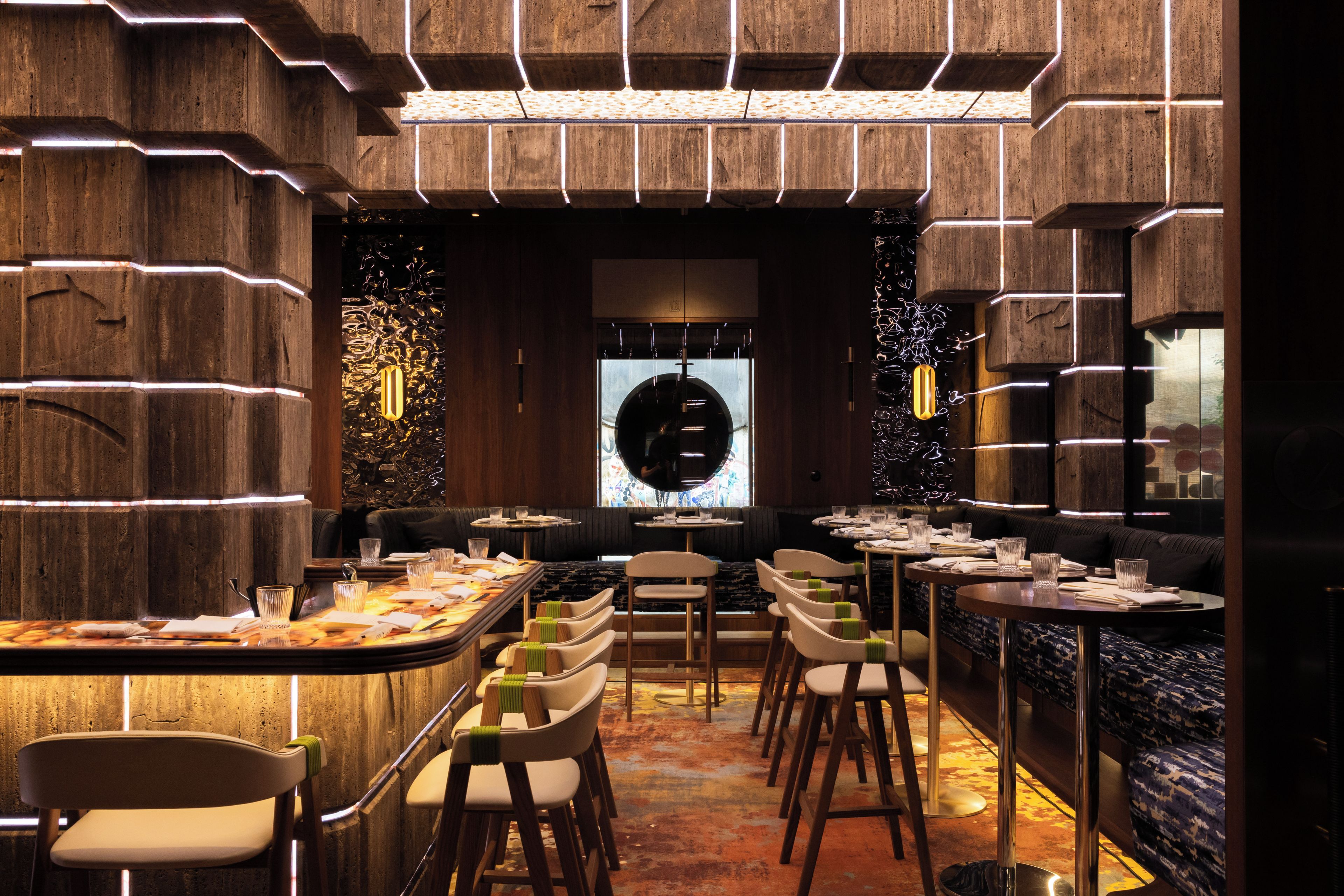 A restaurant interior with a central bar, seating arrangements, and a decorative wall.