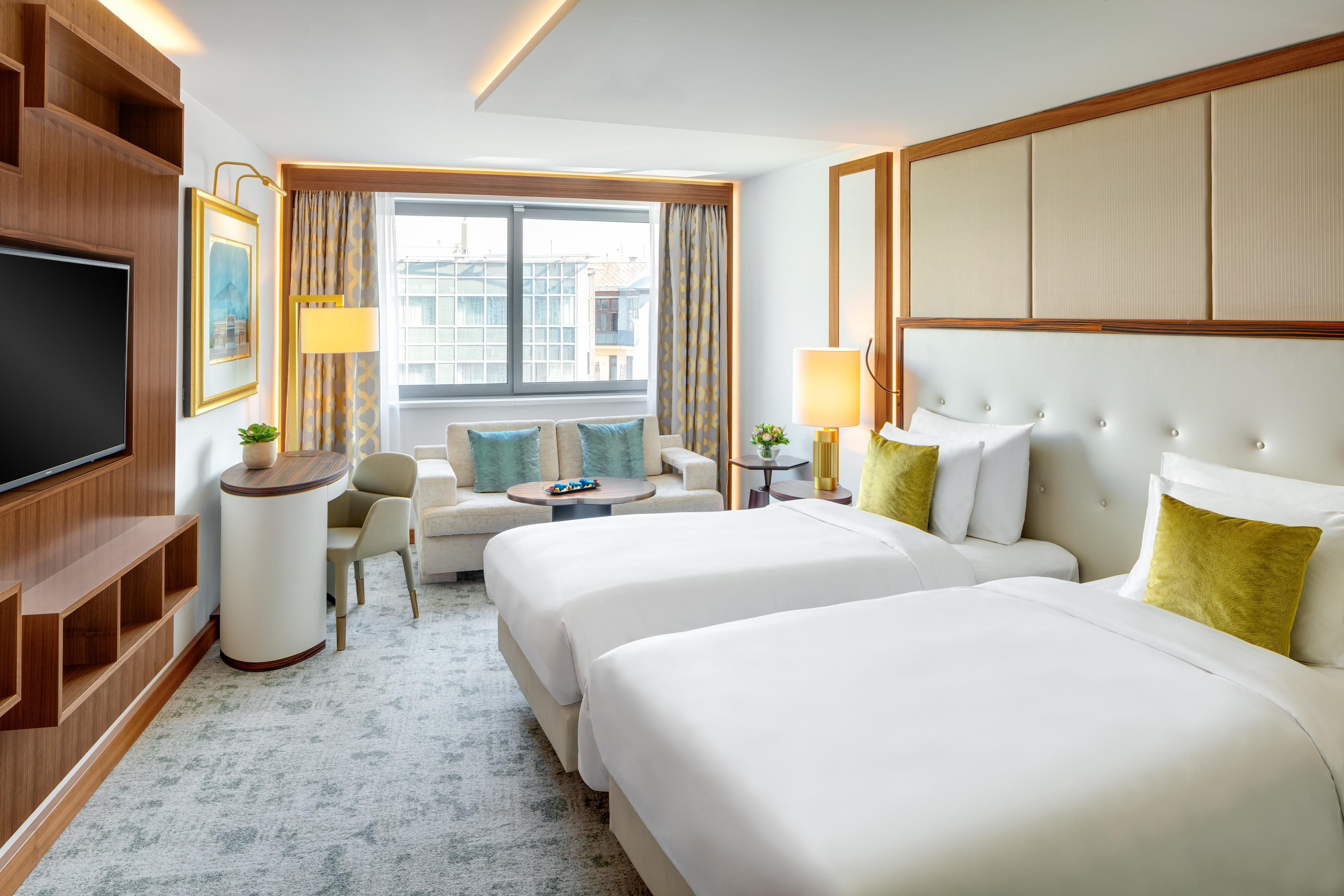 Habitación de hotel con dos camas, un sofá, un televisor y una ventana con cortinas.