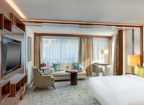 A hotel room with a bed, a sofa, a TV, a coffee table, and a lamp. - Kempinski Hotel Corvinus Budapest (Budapest)