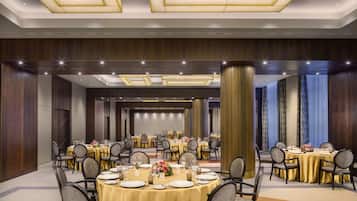 Un amplio salón de banquetes con mesas redondas dispuestas para cenar, destacando un arreglo floral central y un techo alto con iluminación empotrada.