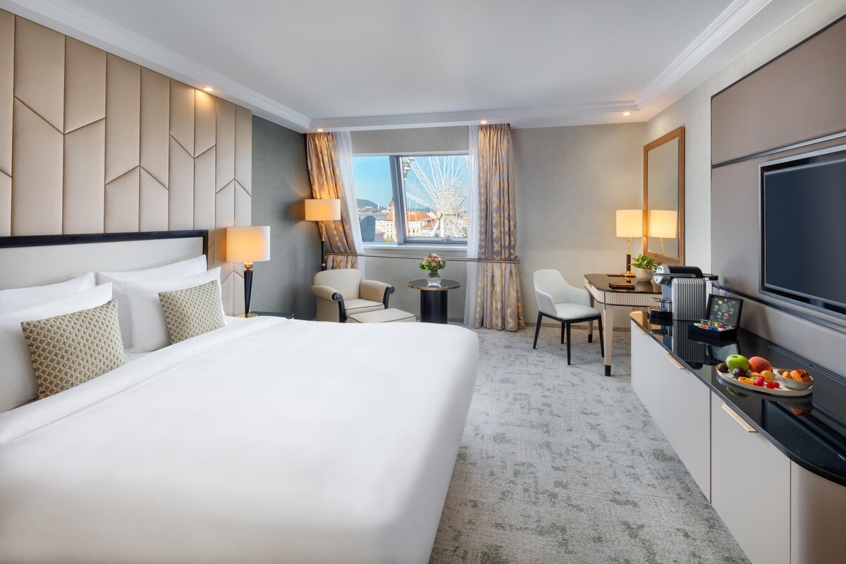 A hotel room with a large bed, a desk, a TV, and a view of a Ferris wheel.