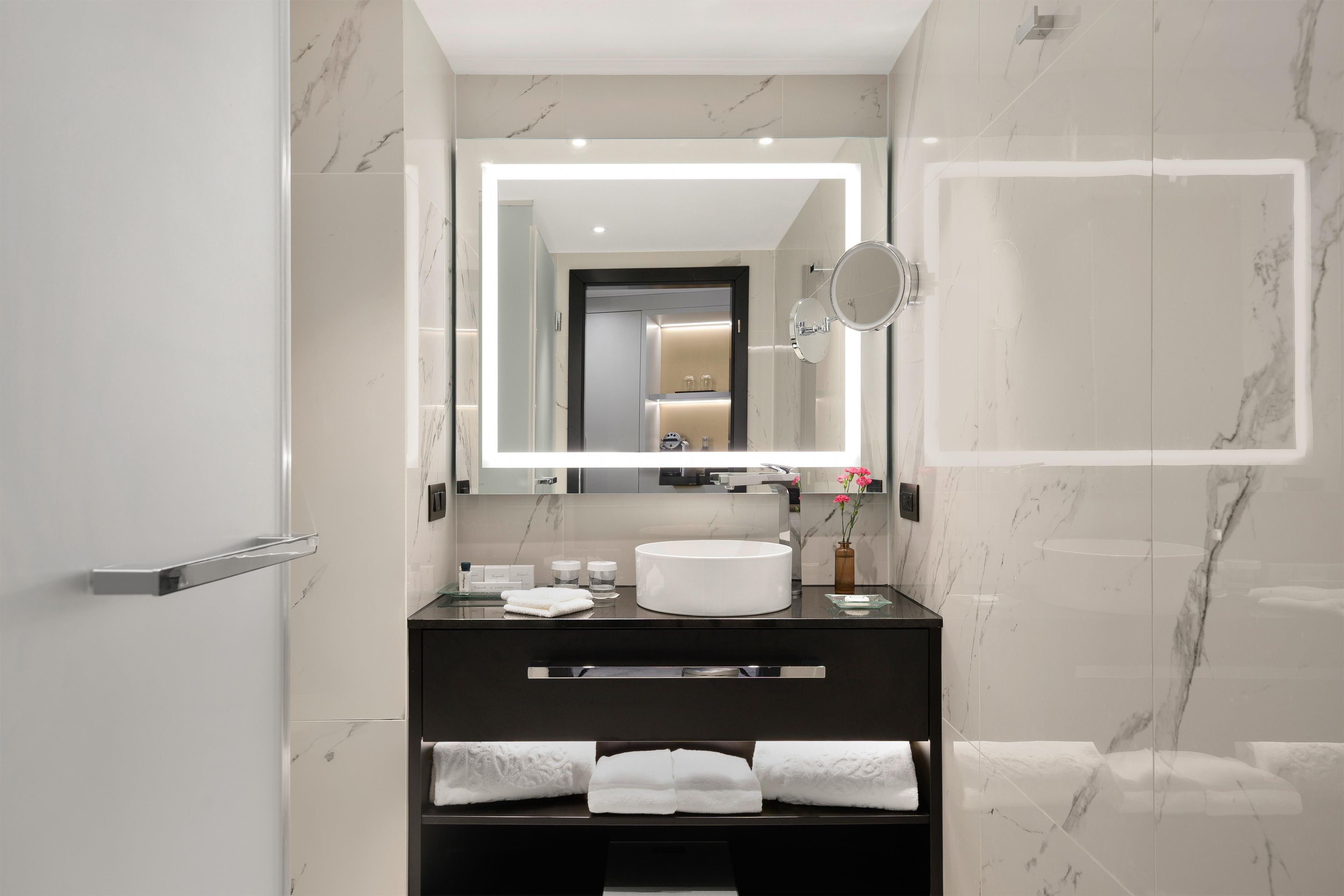 Un baño moderno con pared de mármol, un lavabo redondo, un espejo grande y un perchero para toallas.