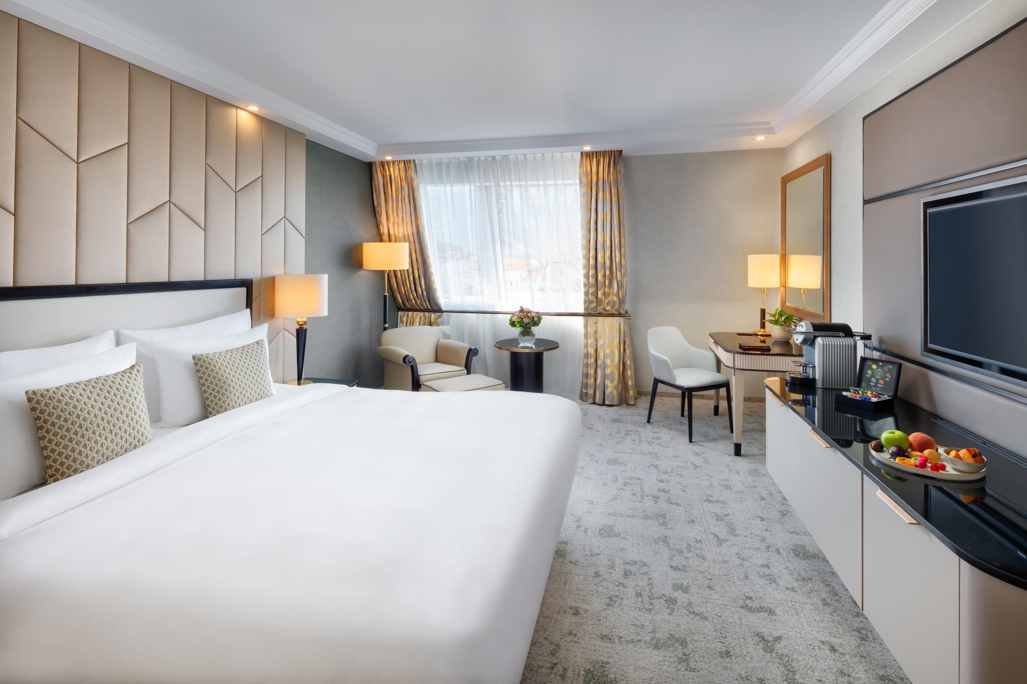Una habitación de hotel con una cama grande, un escritorio con cafetera, un televisor y una mesita con flores.