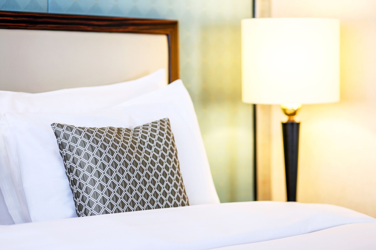A neatly made bed with white and patterned pillows, a wooden headboard, and a bedside lamp.