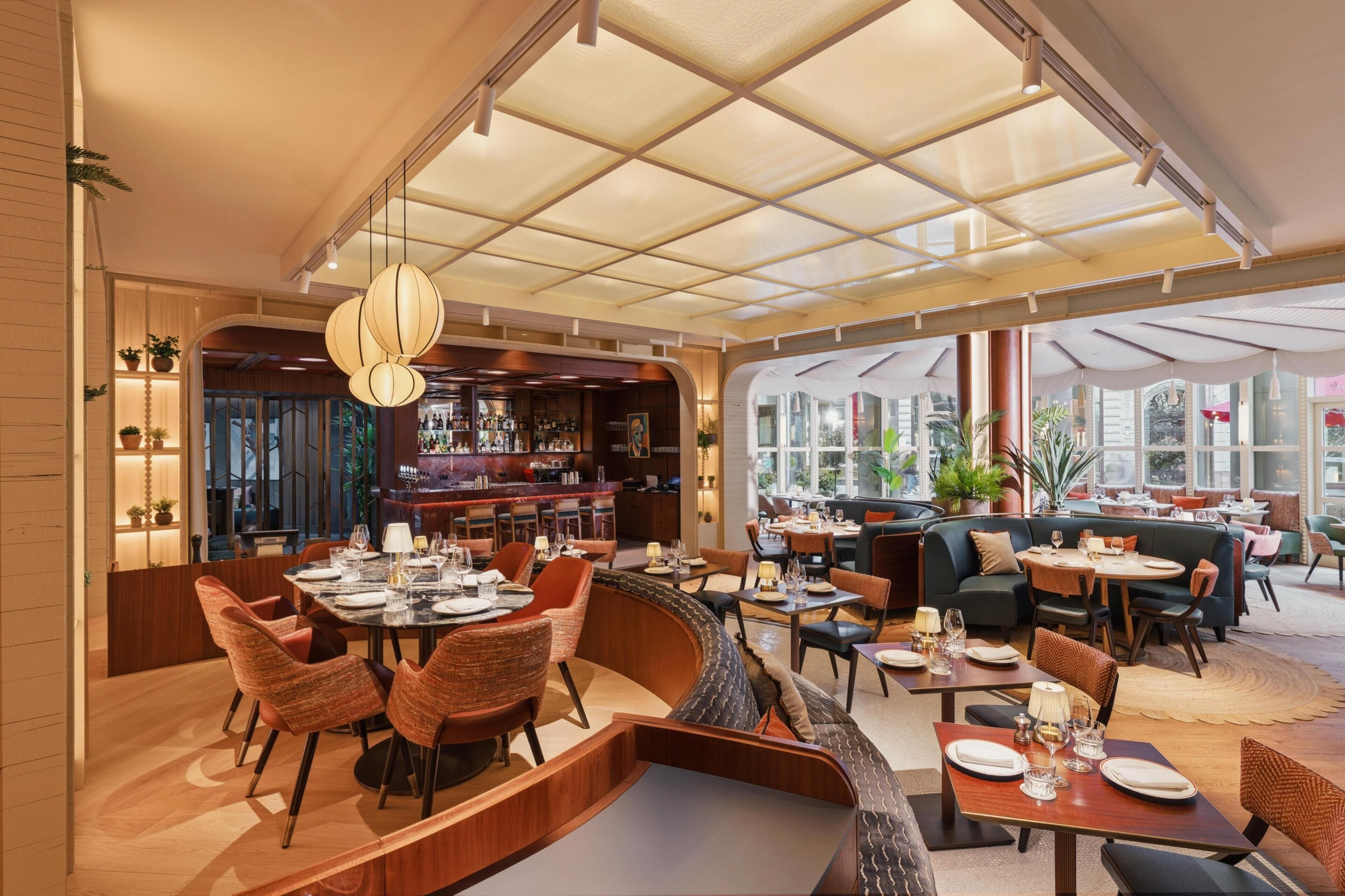 Un restaurant moderne doté d’un bar, de différents types de tables et de grandes fenêtres.