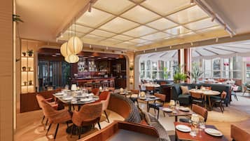 A modern restaurant with a bar area, seating arrangements, and large windows.