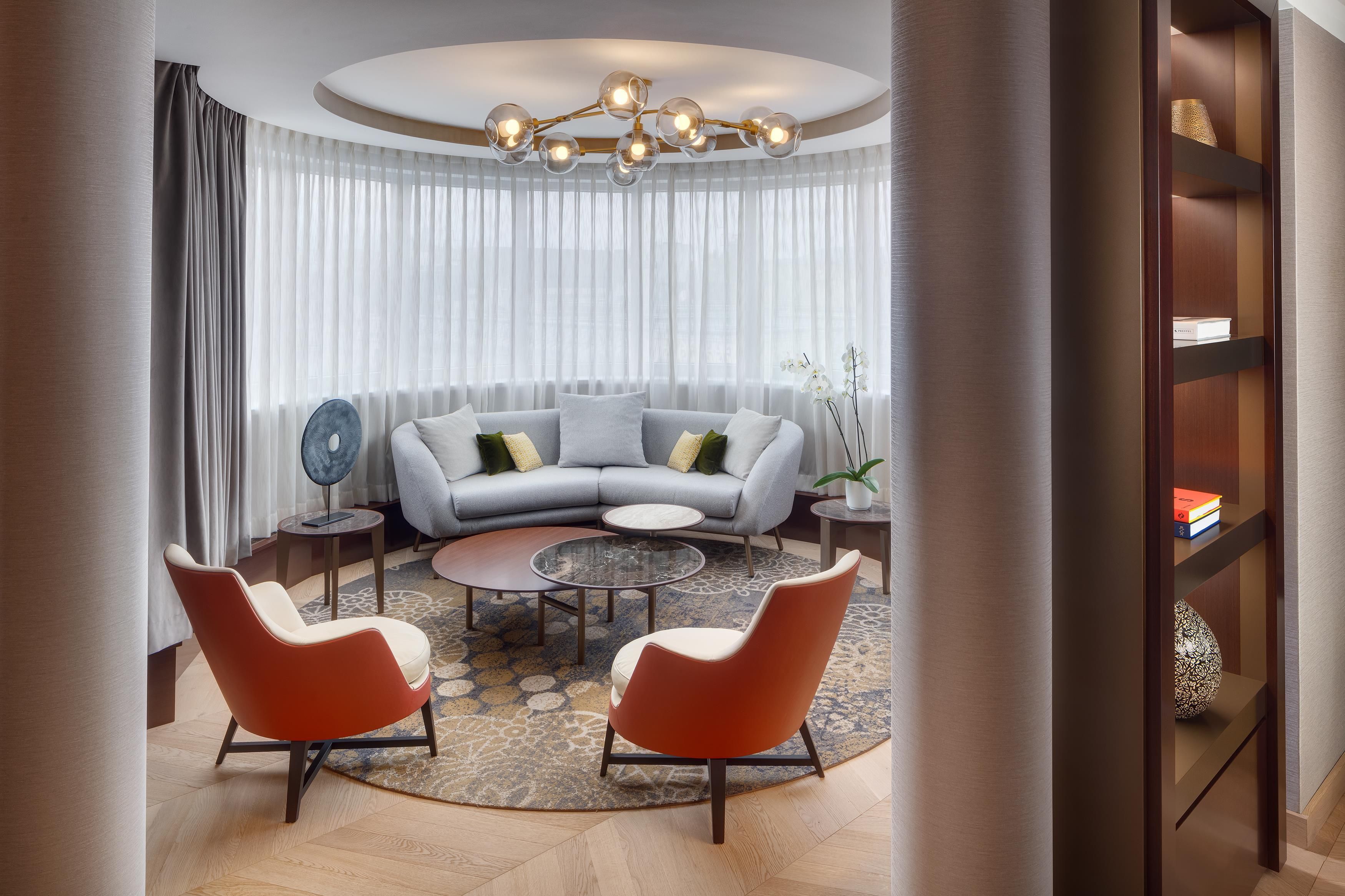 A modern living room with a grey sofa, two armchairs, a coffee table, and a chandelier.