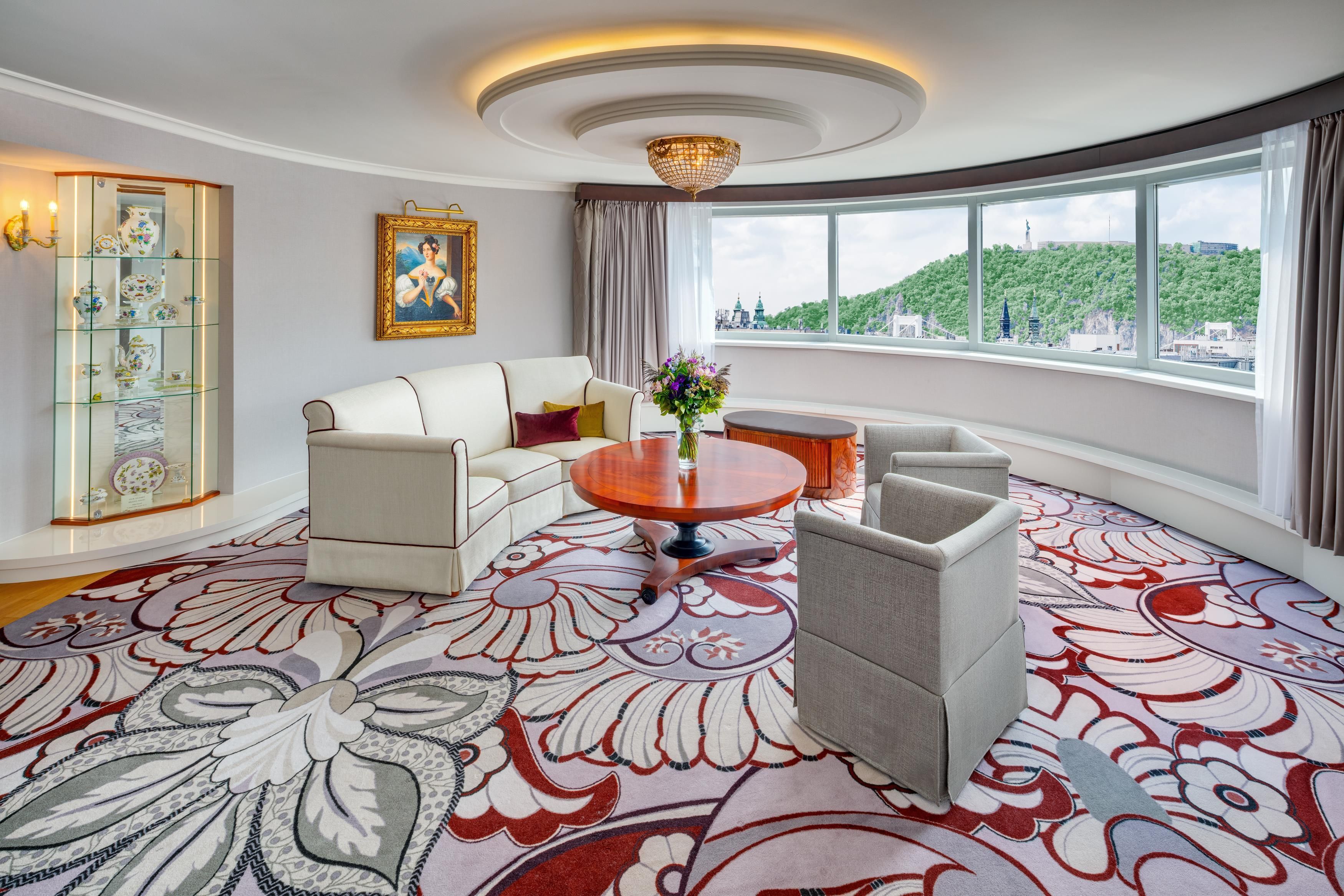 A modern living room with a white sofa, a round coffee table, and a view of a cityscape through large windows.
