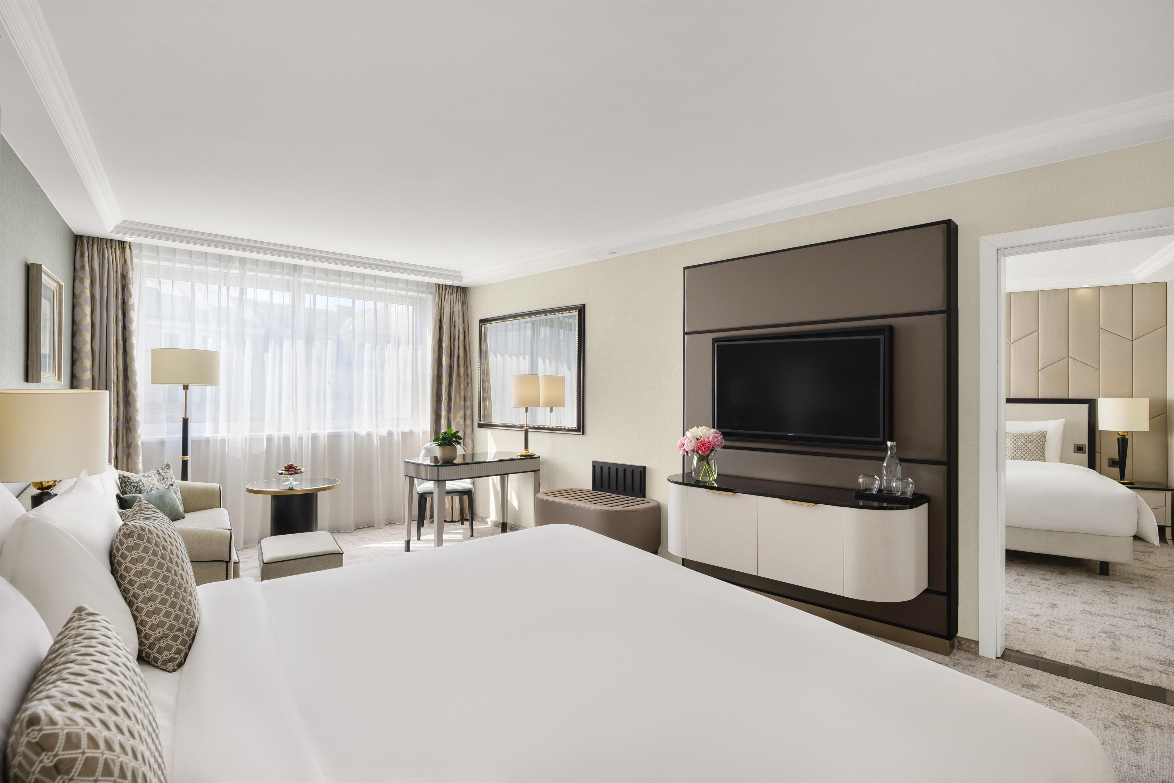 Habitación de hotel con una cama grande, un escritorio con silla, televisión y un baño visible a través de una puerta abierta.