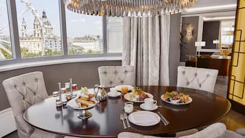 Comedor con una mesa redonda dispuesta para una comida, ventanas amplias con vista a un paisaje urbano y una lámpara de araña moderna.