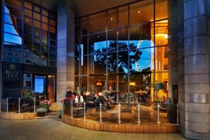 Un hotel moderno con fachada de vidrio, zona de estar al aire libre y un bar visible llamado 'Blue Fox The Bar'.
