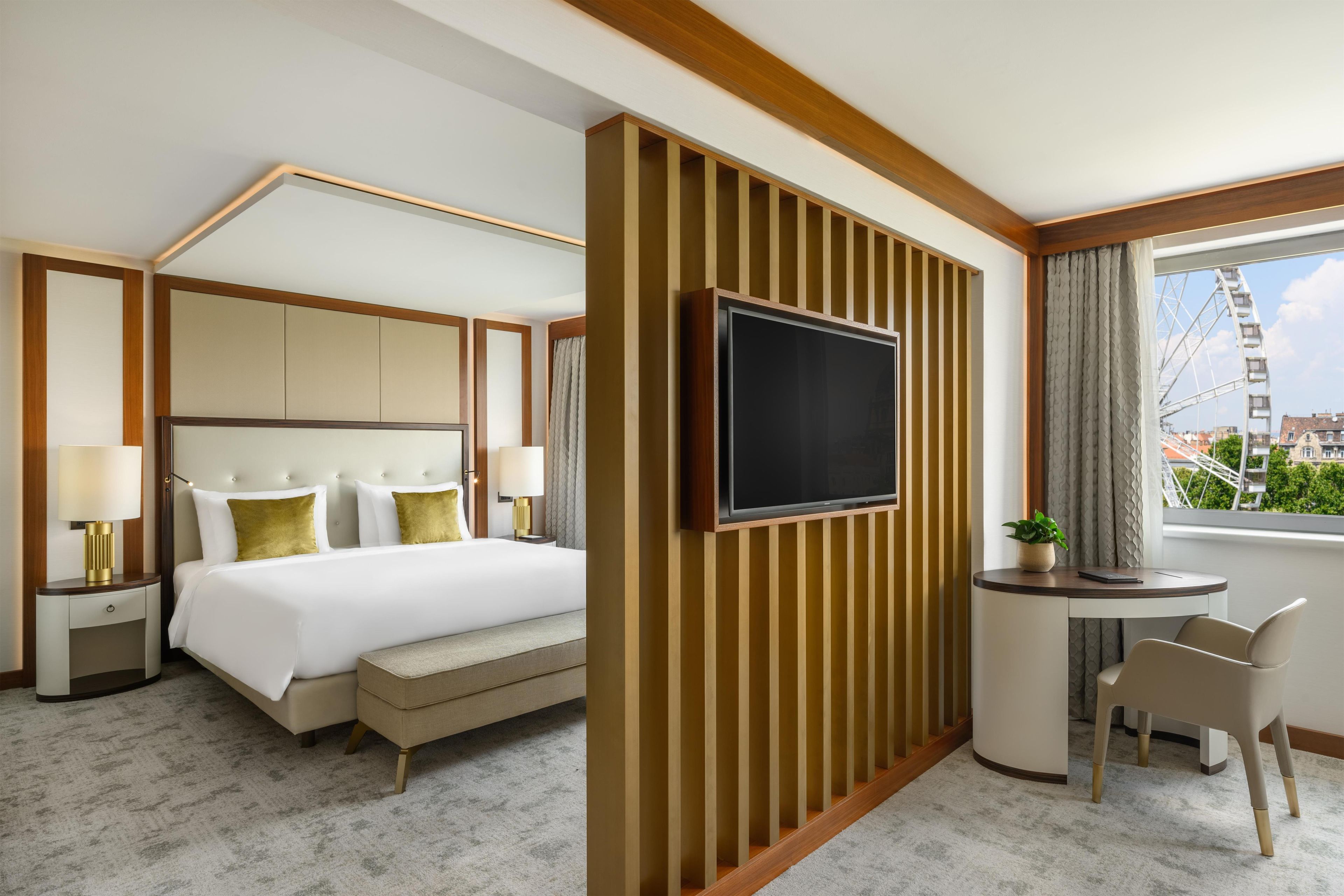 A hotel room with a bed, a TV, a desk with a chair, and a view of a Ferris wheel.