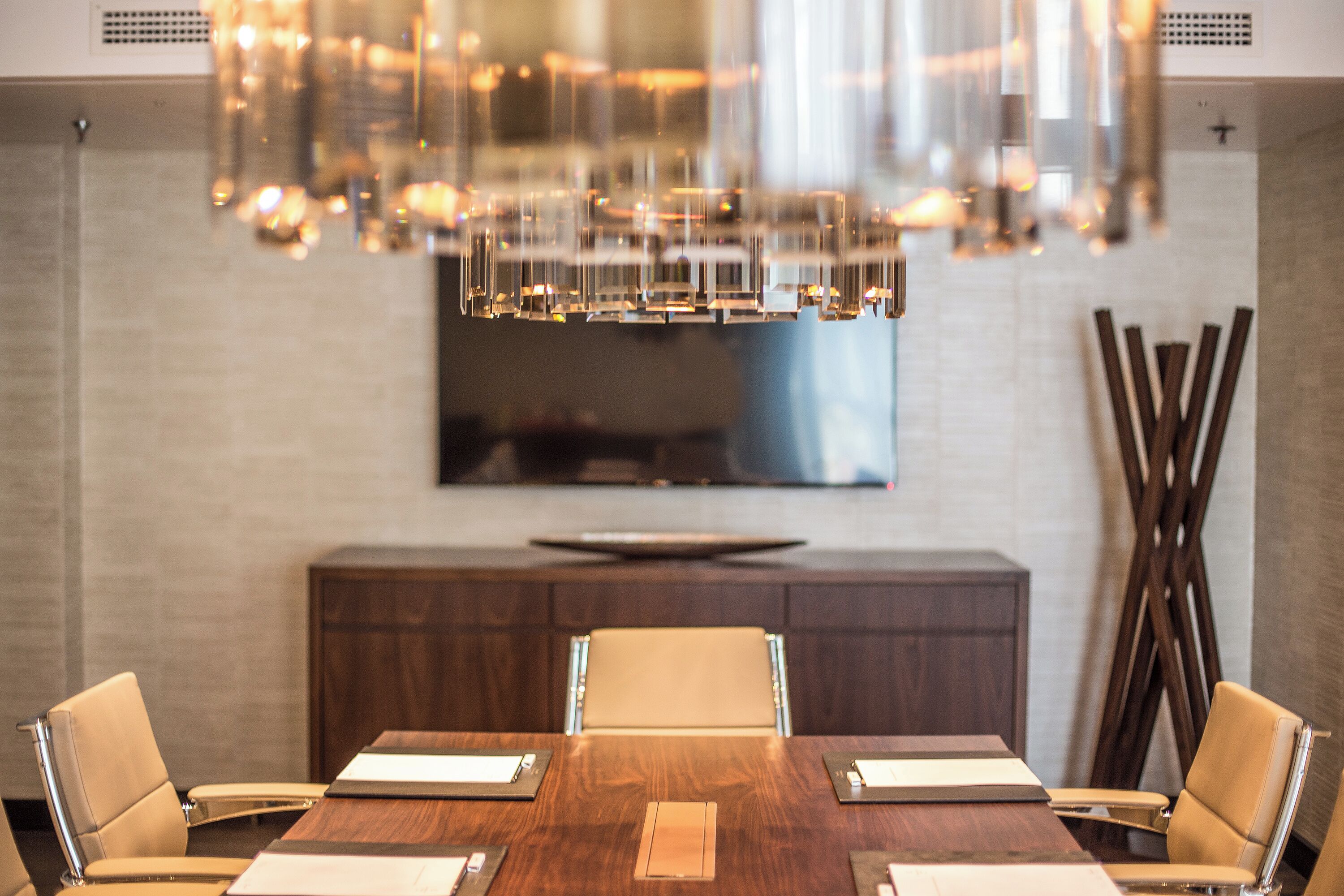 Un comedor moderno con mesa de madera, sillas de cuero y una lámpara de araña grande.