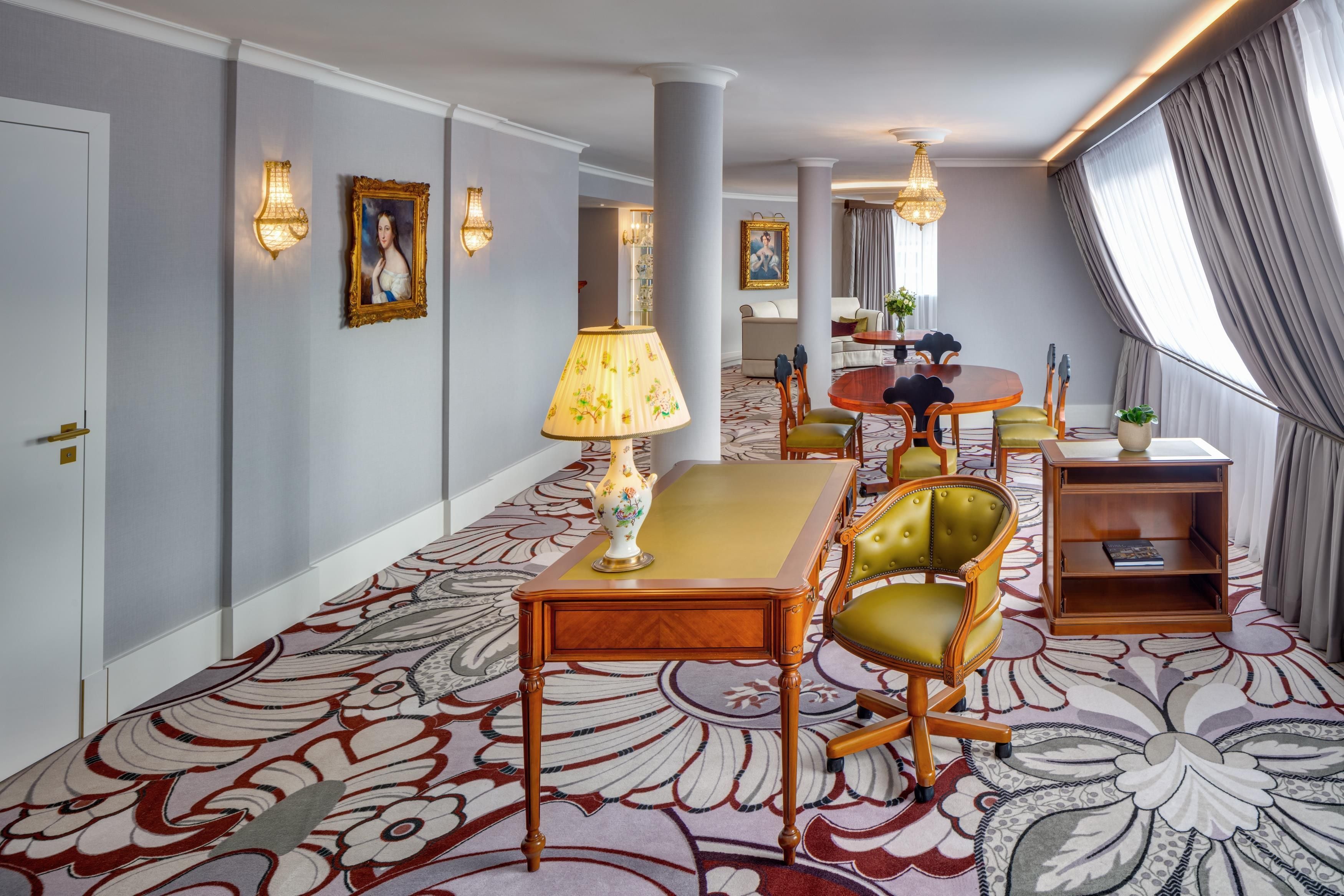 Una habitación de hotel con alfombra estampada, una mesa de comedor con sillas, un sofá y una estantería.