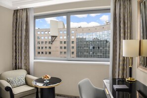 A hotel room with a curved window, a sofa, a small round table with a glass top, and a lamp. - Kempinski Hotel Corvinus Budapest (Budapest)