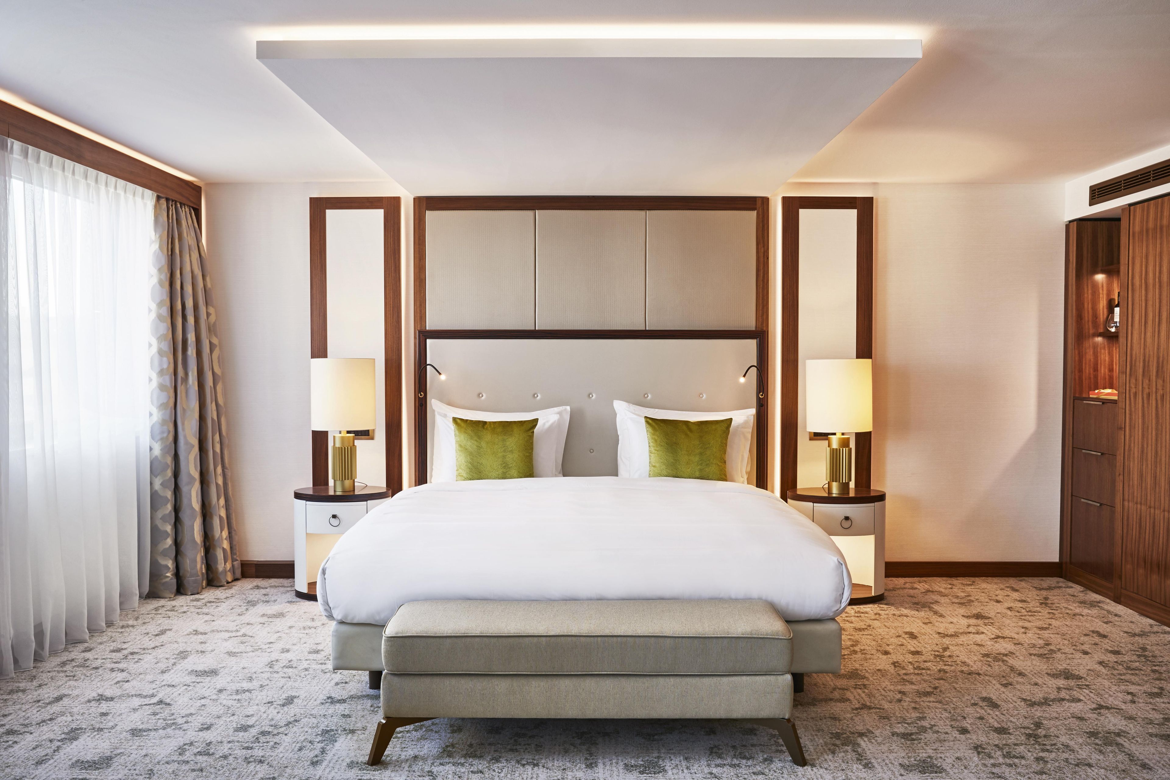 A hotel room with a large bed, two bedside tables with lamps, a bench at the foot of the bed, and a wardrobe.