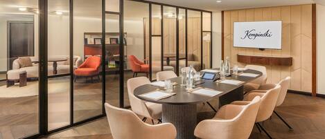 Una sala conferenze moderna con un ampio tavolo, sedute confortevoli e uno schermo televisivo che mostra il nome "Kempinski".