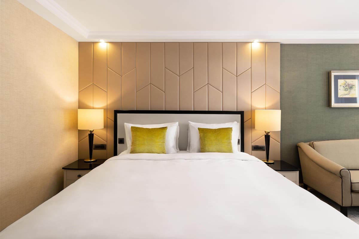 Hotellihuone, jossa on suuri sänky, kaksi yöpöytävalaisinta, tuoli ja seinä, jossa on geometrinen kuvio.