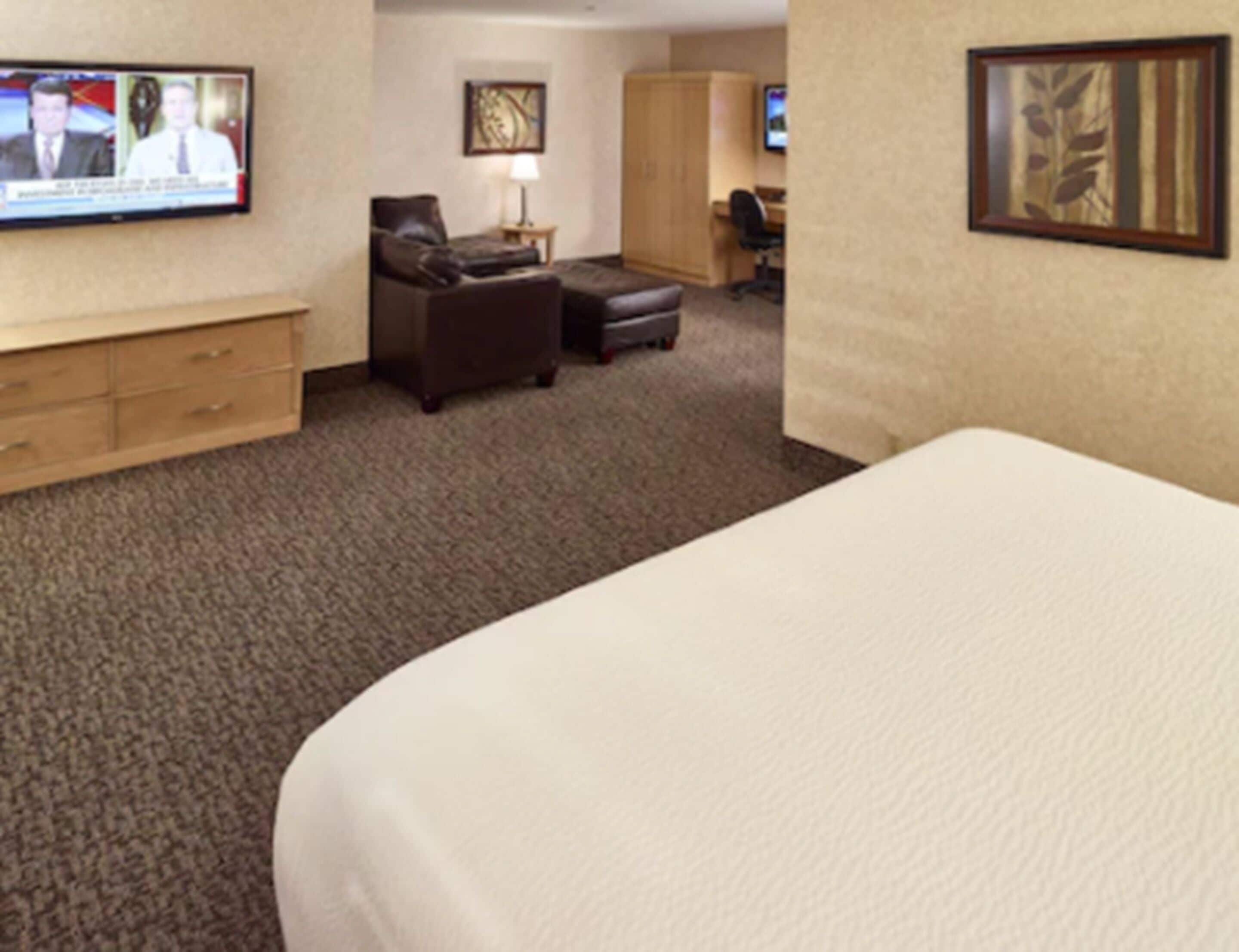 A hotel room with a large bed, a desk, a chair, a sofa, and a television on the wall.