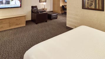 A hotel room with a large bed, a desk, a chair, a sofa, and a television on the wall.