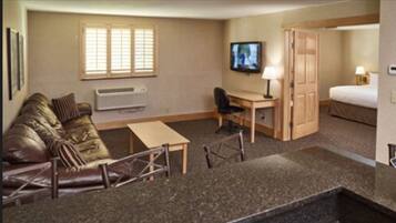 A compact hotel room with a sofa, a desk, a television, a bed, and a small kitchenette.