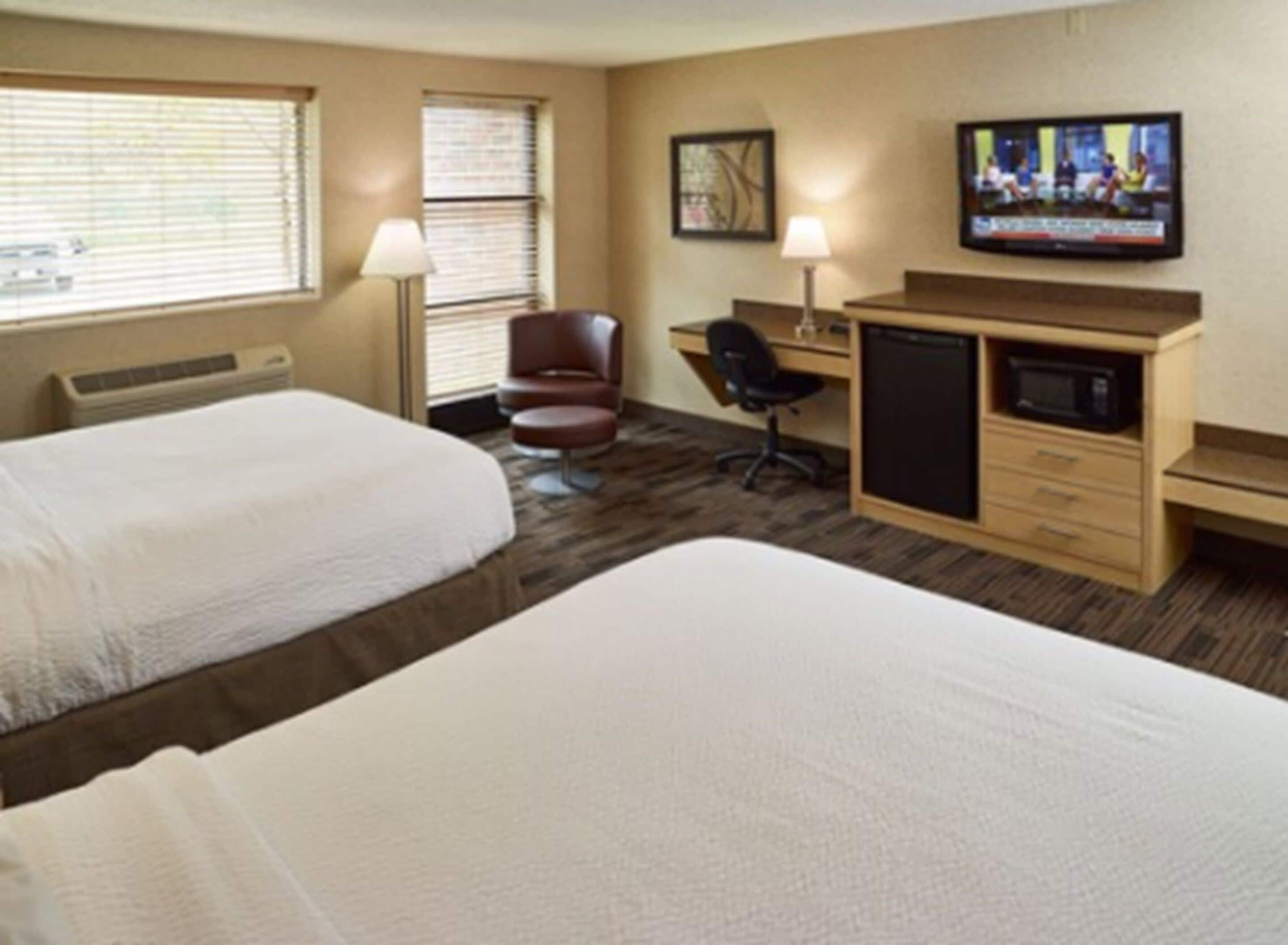Habitación de hotel con dos camas, un escritorio con computadora, una silla, televisor y microondas.