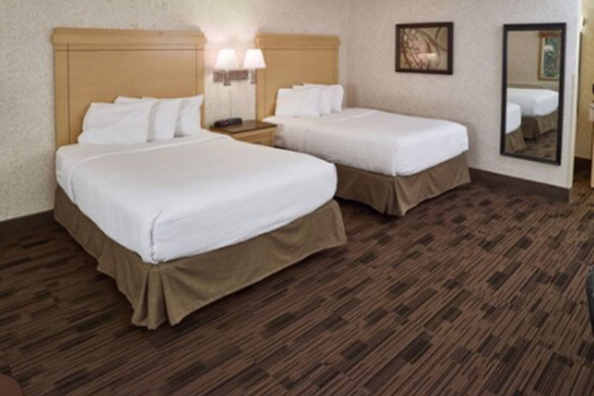 Una habitación de hotel con dos camas, cabecero de madera, lámparas de noche y un espejo en la pared.