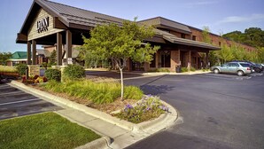 A hotel with a prominent sign, a parking lot, and a landscaped area with trees and flowers.