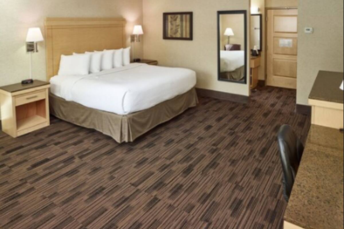 Una habitación de hotel con una cama grande, mesitas de noche, un escritorio y un espejo.