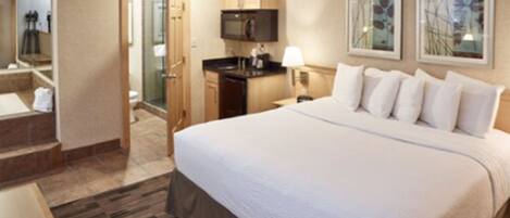 Ein Hotelzimmer mit einem großen Bett, einem Badezimmer mit Dusche, einer kleinen Küchenzeile und einem Spiegel.