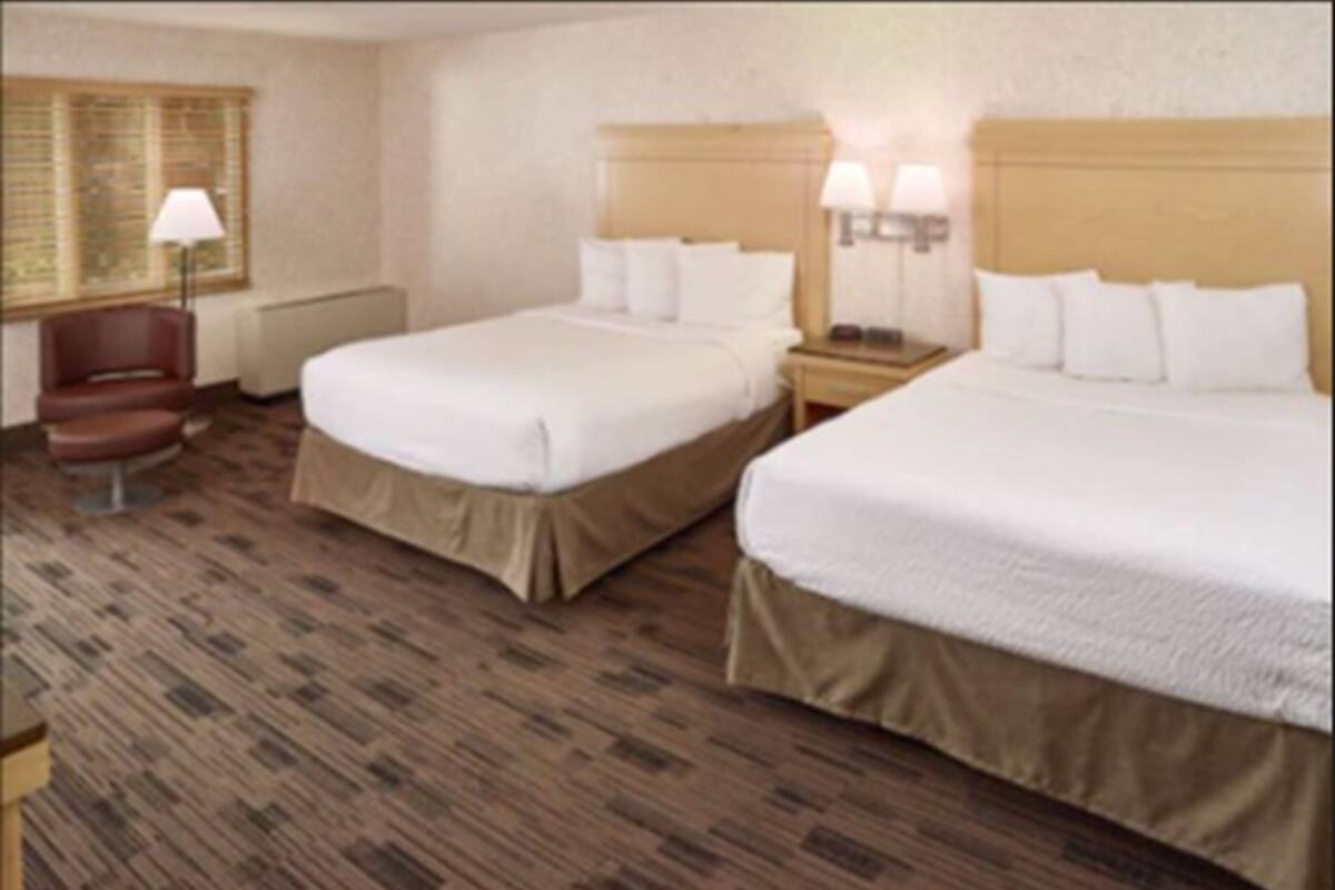 Habitación de hotel con dos camas, una silla, una lámpara y una ventana con persianas.