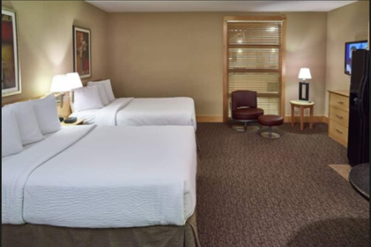 Una habitación de hotel con dos camas, una silla, una mesita y un televisor.