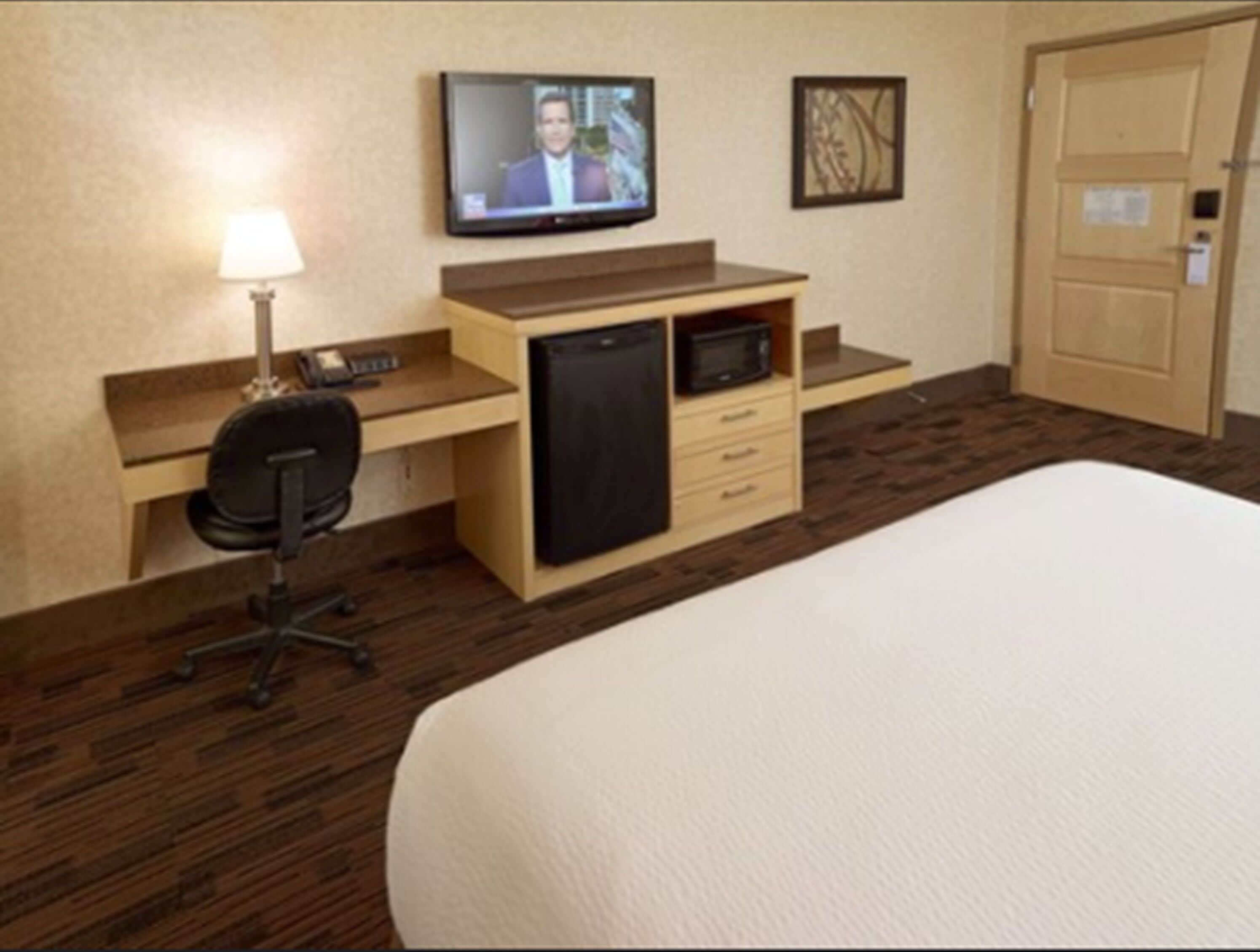 Una habitación de hotel con cama, escritorio con computadora, televisor, microondas y puerta.