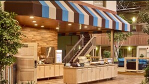 A spacious indoor area with a wooden counter, a striped awning, and a staircase leading to an upper level.