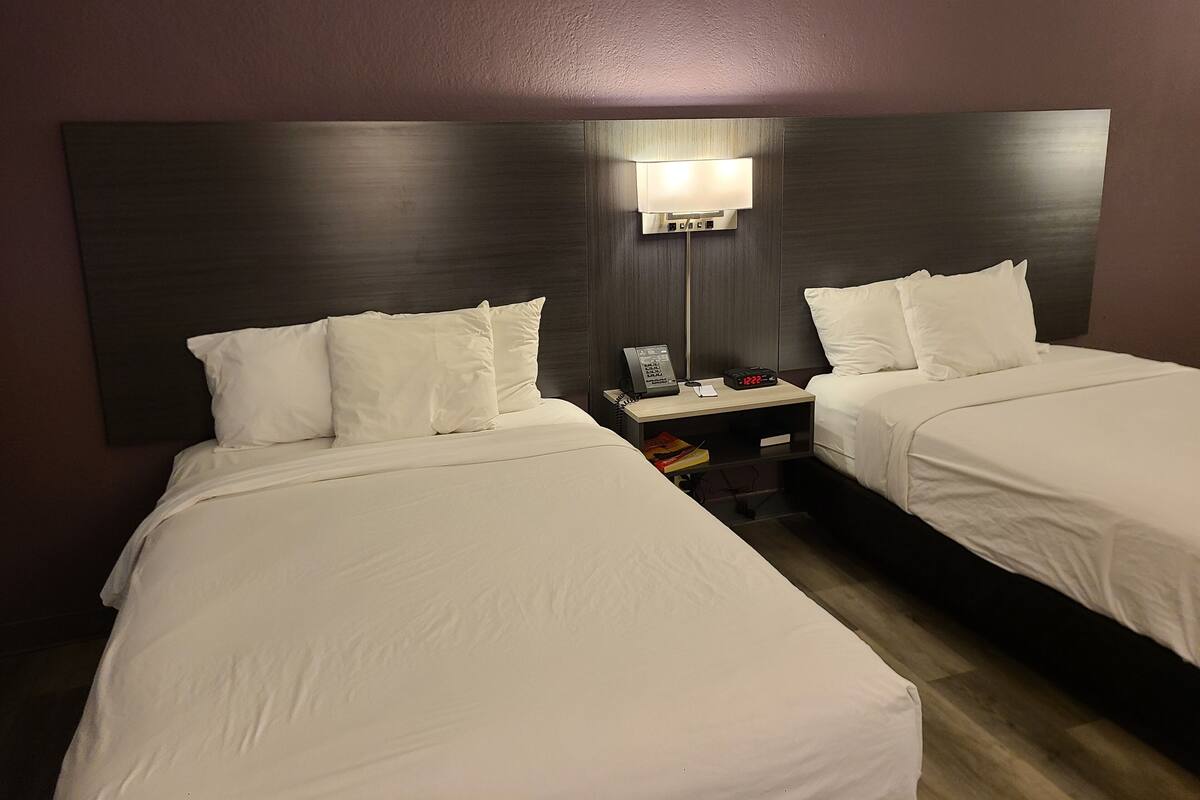 Una habitación de hotel con dos camas, una mesita de noche con lámpara y un teléfono en la pared.