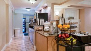 A hotel kitchen with a buffet area featuring fruits, pastries, and a coffee machine. - La Quinta Inn by Wyndham Farmington (Farmington)