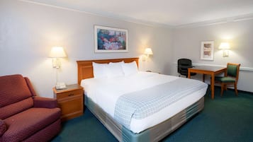 A hotel room with a bed, a desk, a chair, and a telephone on a nightstand.