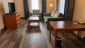 A hotel room with a wooden floor, a television on a dresser, a sofa, a small table, and a lamp. - La Quinta Inn by Wyndham Farmington (Farmington)