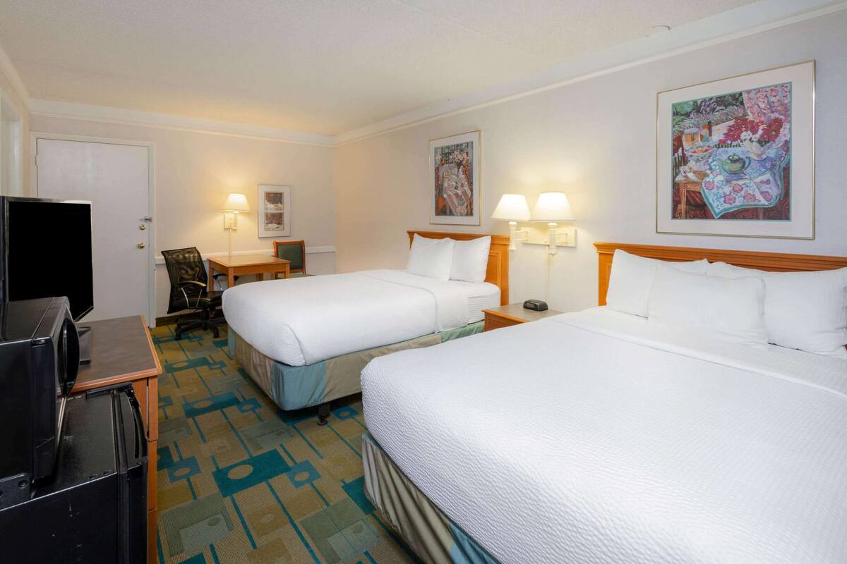 Una habitación de hotel con dos camas, un escritorio, un televisor y una mesa de comedor.