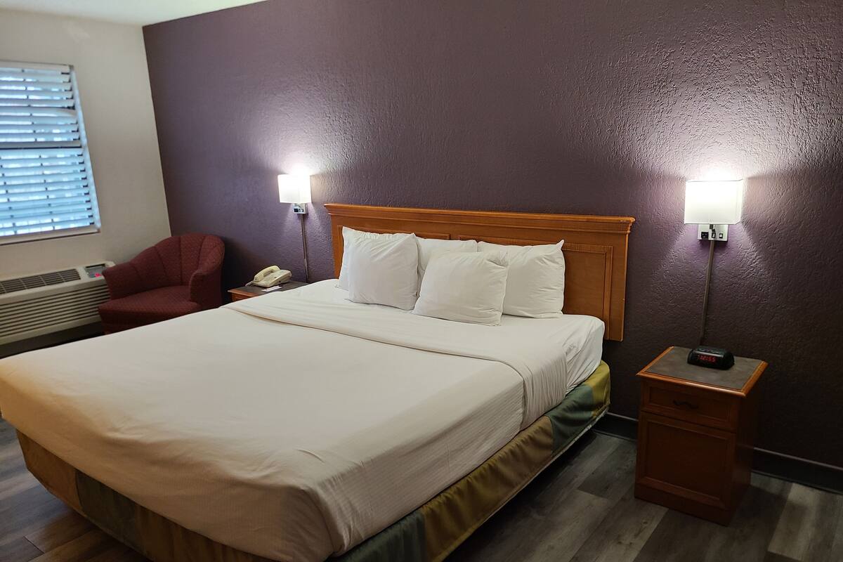 Habitación de hotel con cama, lámparas de noche, mesita de noche, una silla y un calentador de pared.
