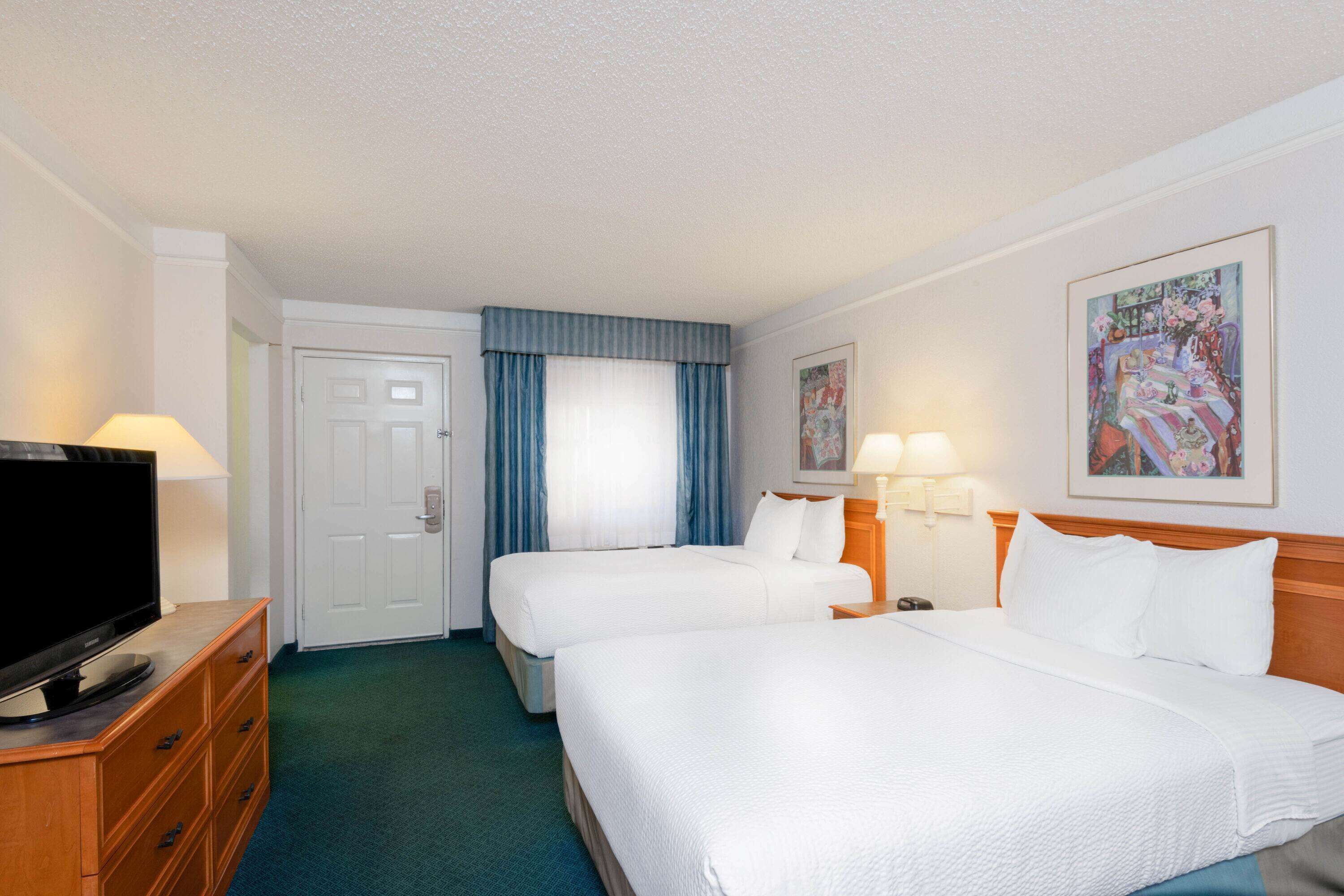 A hotel room with two beds, a TV, a dresser, and a painting on the wall.
