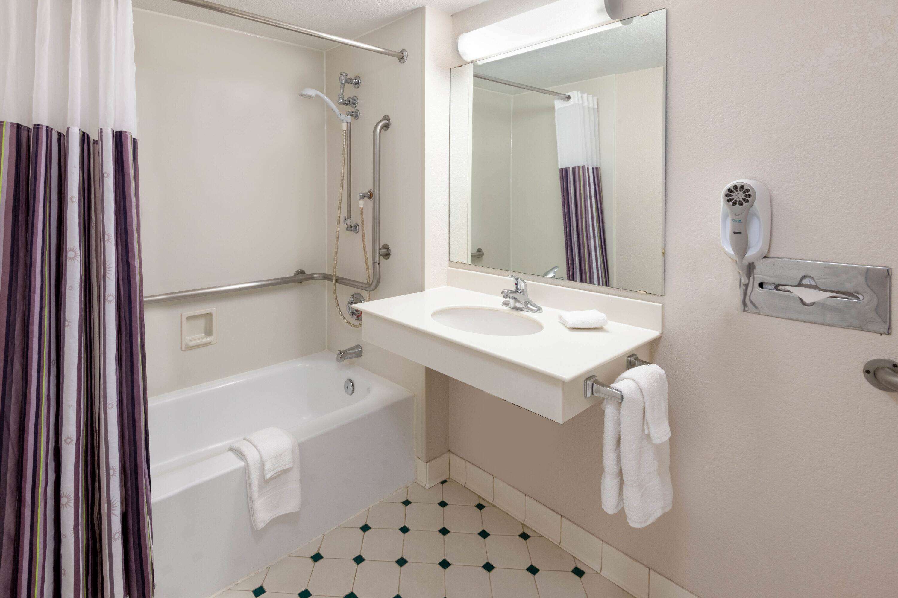 A bathroom with a bathtub, a sink, a mirror, and a hairdryer.