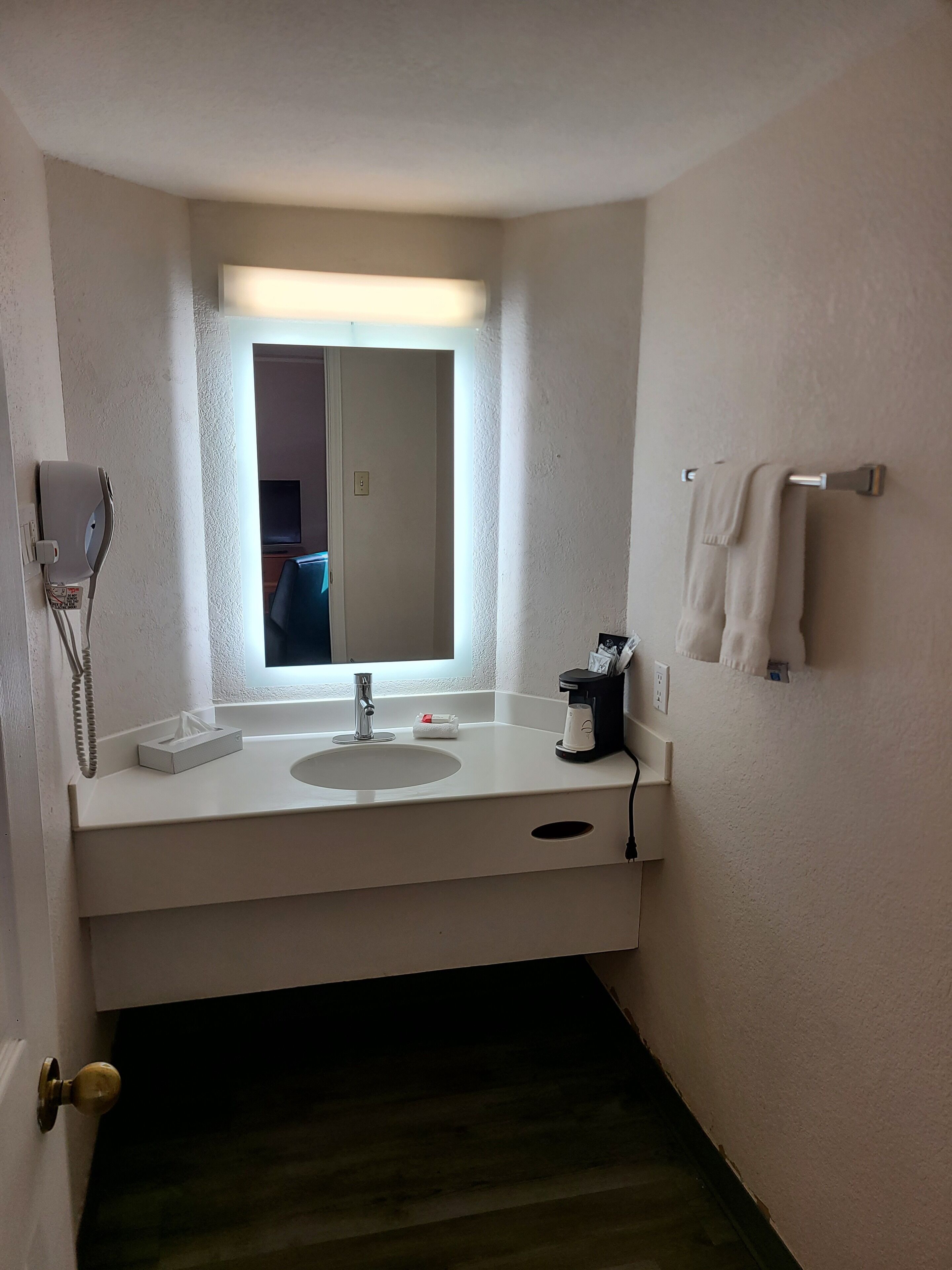 Une salle de bain avec un lavabo blanc, un miroir au-dessus, un porte-serviettes et un téléphone.