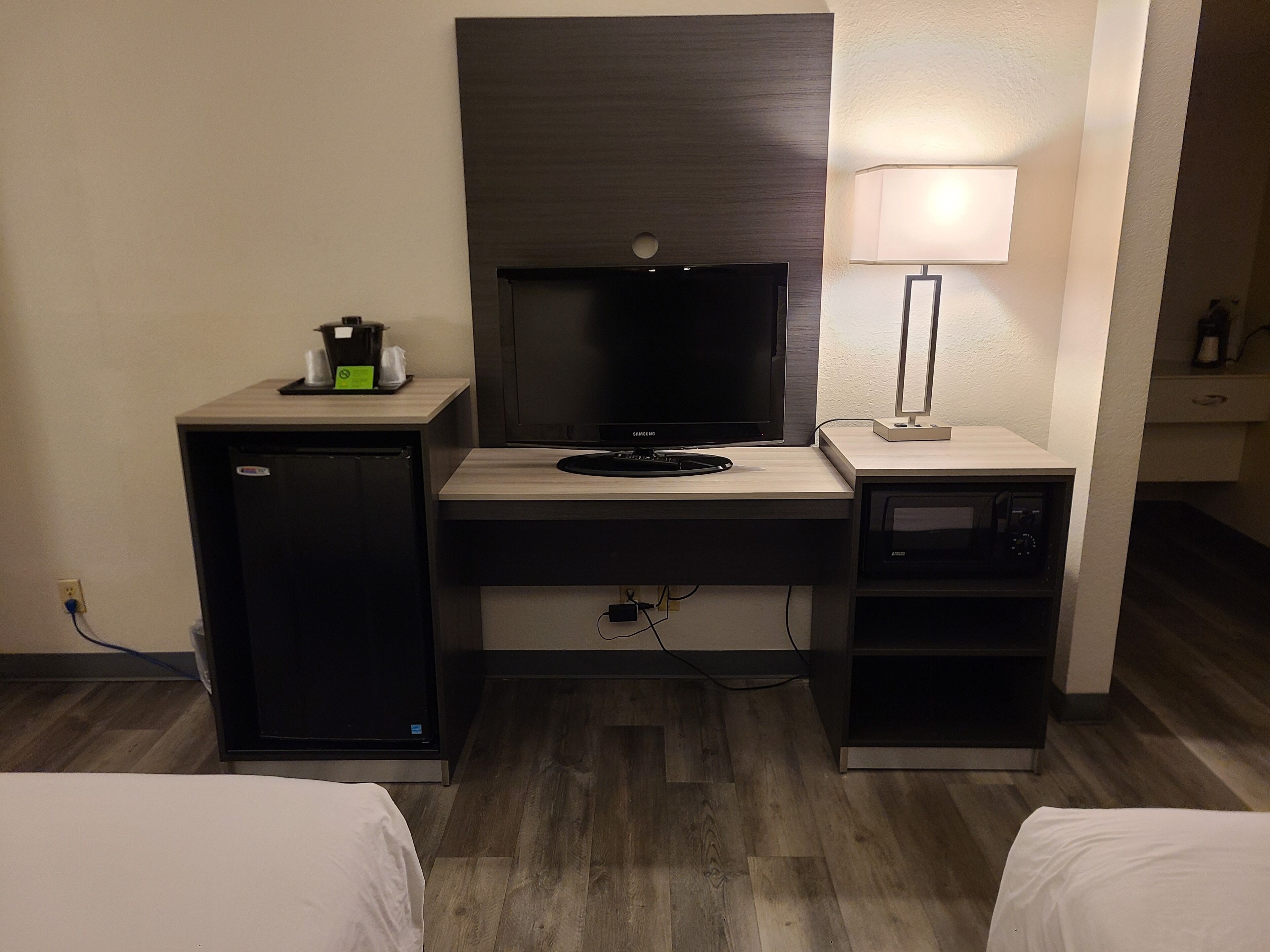 A compact hotel room with a kitchenette, a television, a lamp, and a microwave.