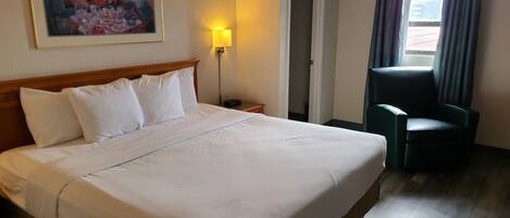 A hotel room with a large bed, a chair, a painting on the wall, and a lamp.