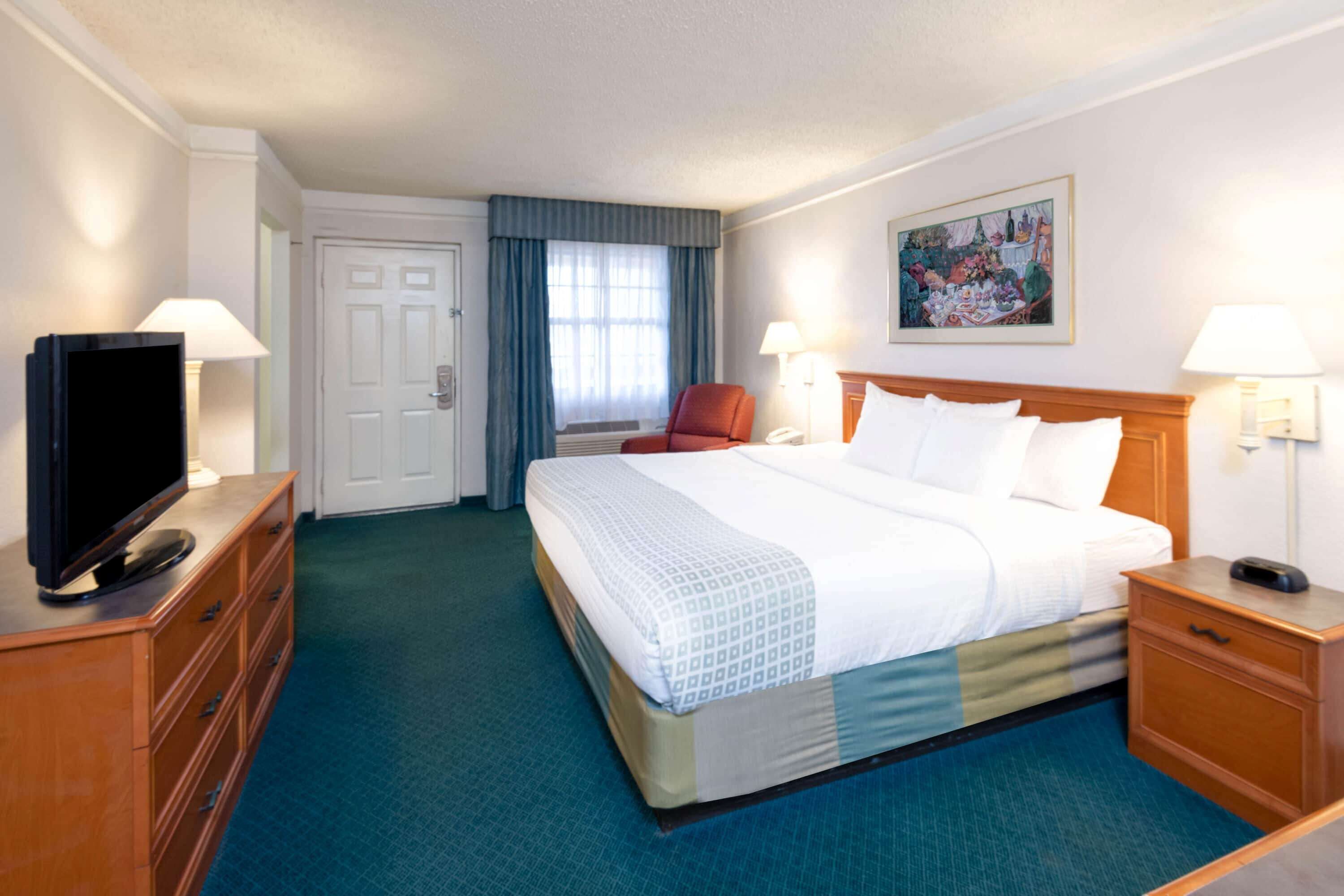 Een hotelkamer met een groot bed, een televisie op een dressoir, een bureau met een lamp en een schilderij aan de muur.