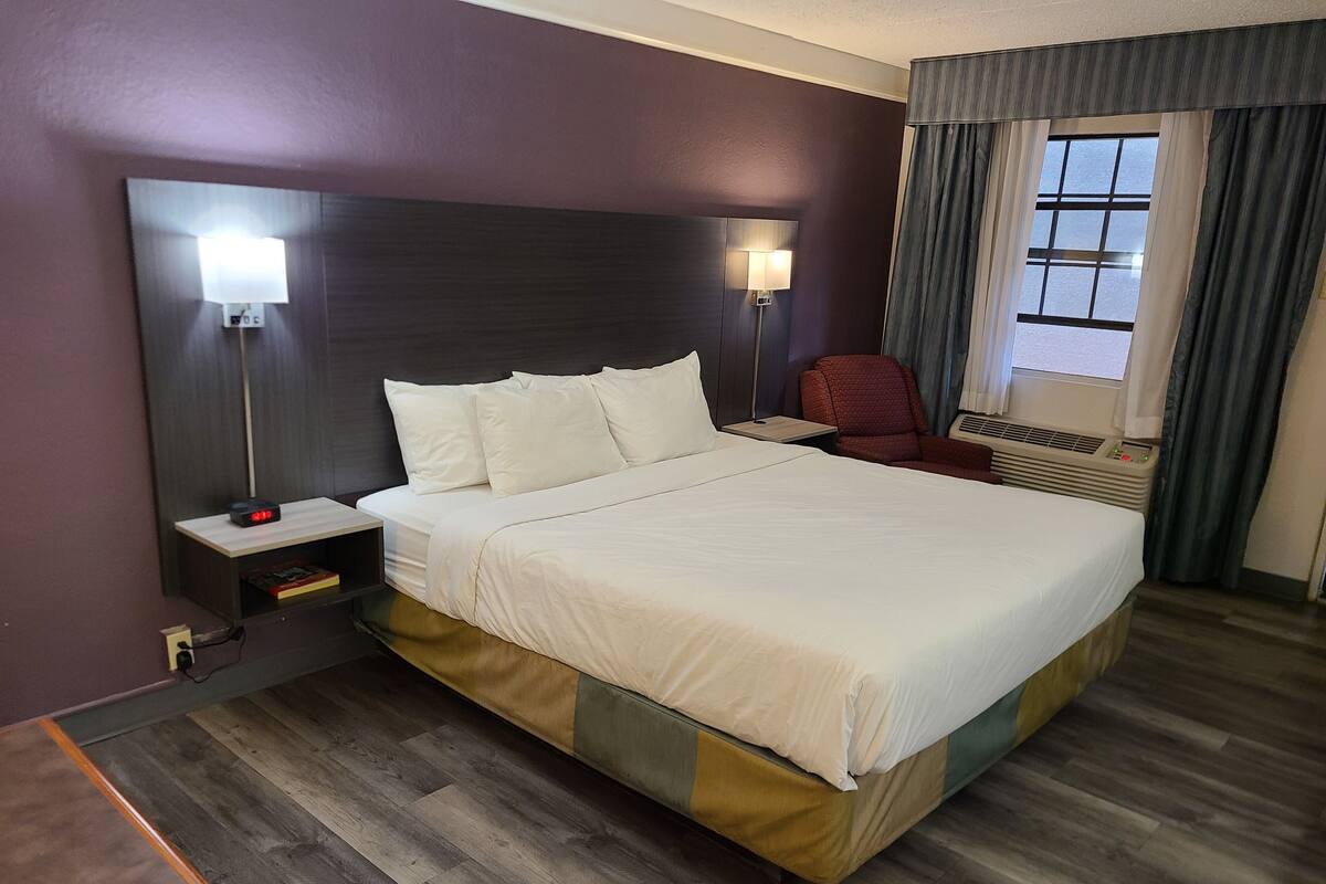 Habitación de hotel con una cama grande, dos lámparas de noche, una silla, una mesita de noche y una ventana con cortinas.